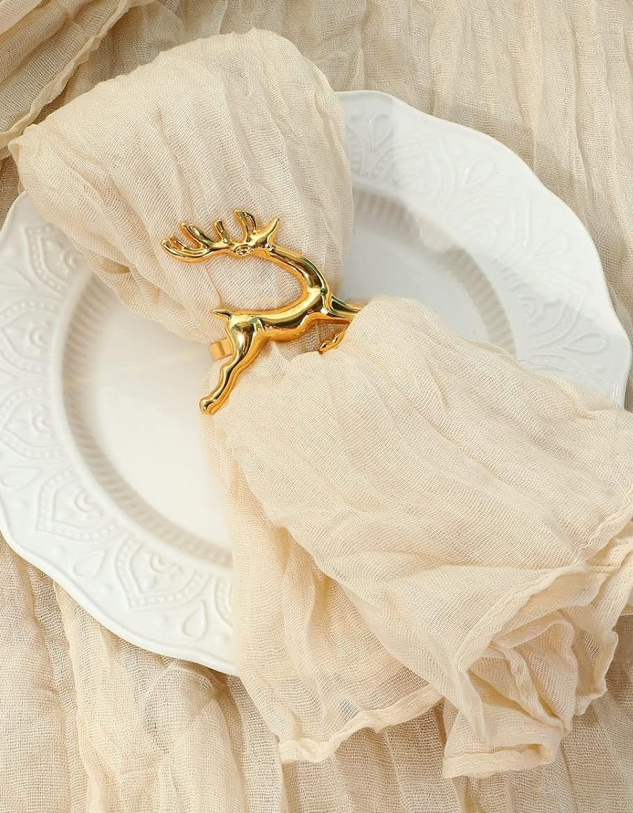 Cremefarbene Musselinserviette in einem goldenen Ring in Zweigform auf einem weißen Teller