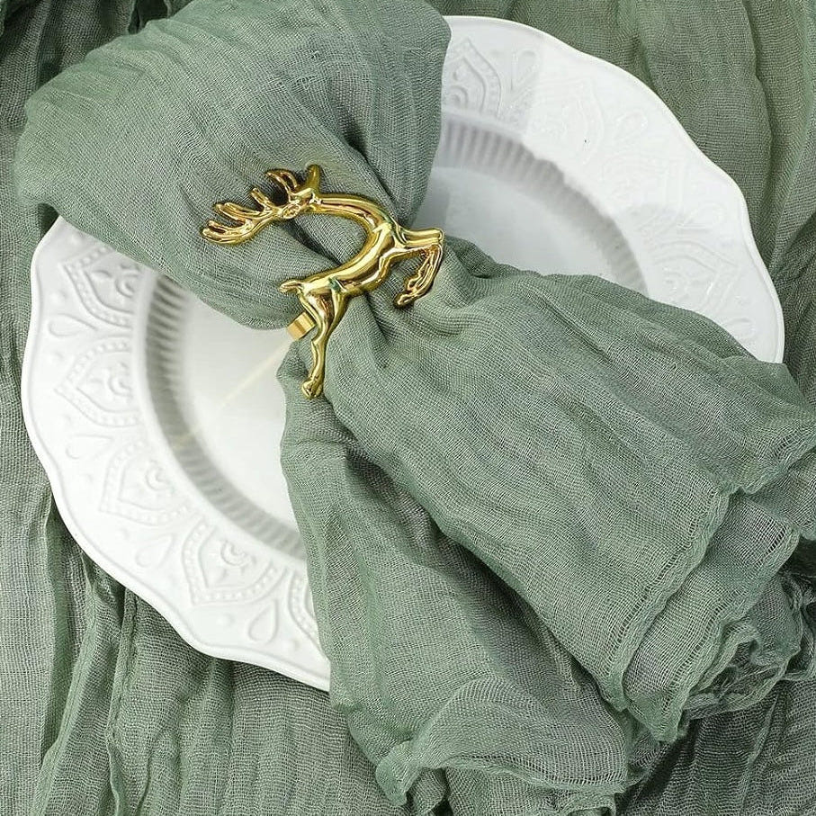 Salbeigrüne Musselinserviette in einem goldenen Ring in Zweigform auf einem weißen Teller