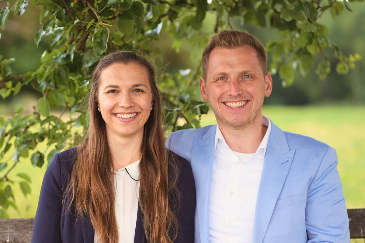 Sara und Lukas, die Gründer von Eventzauber, sitzen lächelnd auf einer Bank unter einem Baum