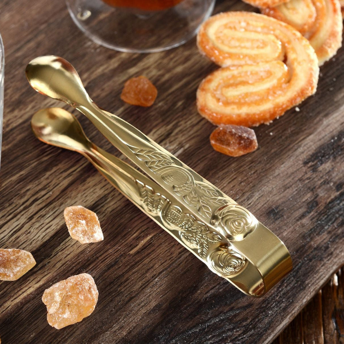 Goldene Zange auf einem Holzbrett mit Kandiszucker und einer Tasse Tee