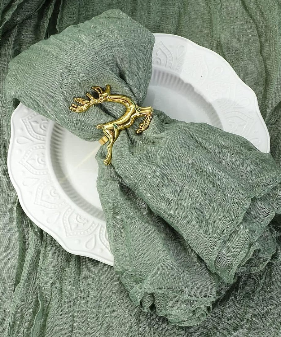 Salbeigrüne Musselinserviette in einem goldenen Ring in Zweigform auf einem weißen Teller